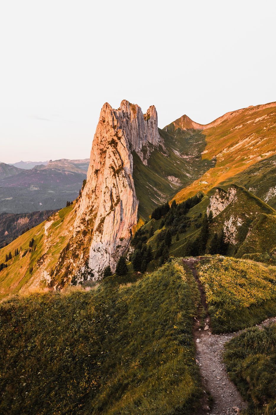 Rock towers at the Saxer Lücke glowing in the evening light, with a trail along the green ridge.