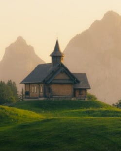 A wooden chapel on a meadow below the mountains