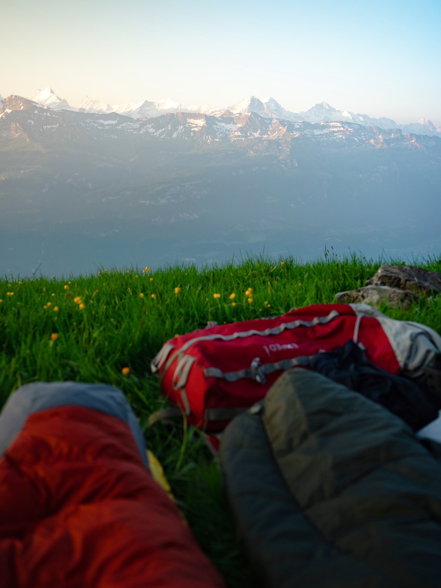 Sacs de couchage sur l'herbe alpine à l'heure dorée avec vue sur les sommets enneigés