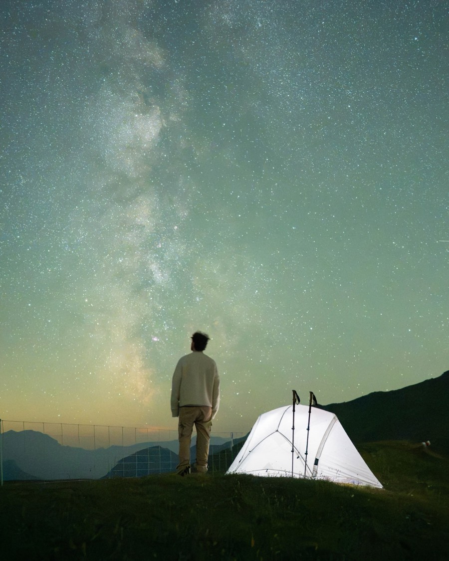 Milky Way over a lit tent on an alpine ridge at night